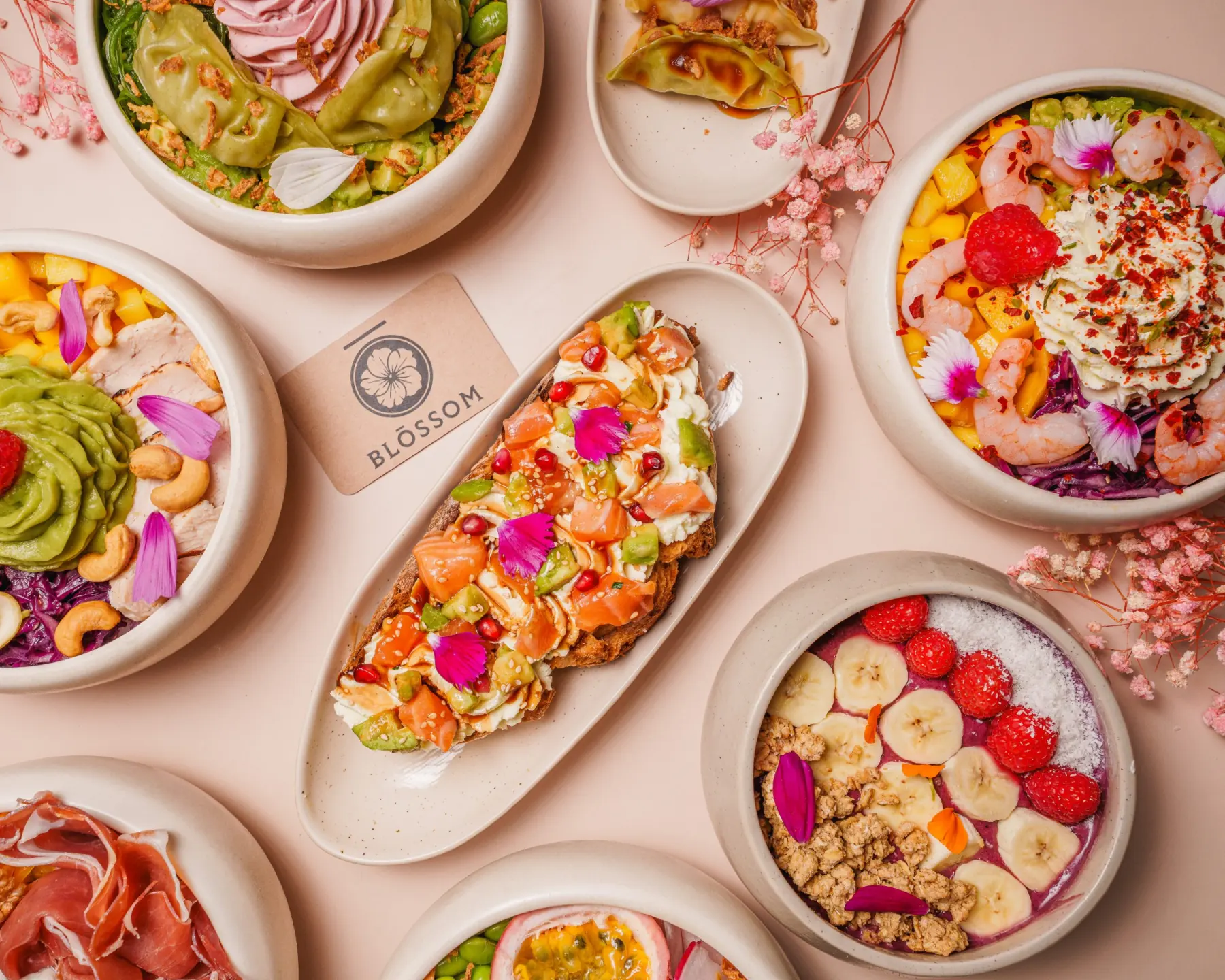 Table de brunch BLŌSSOM vue du dessus : bowls, toasts et boissons sur fond rose poudré